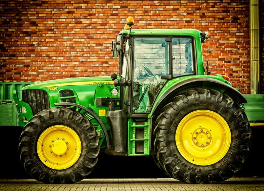 Green farm tractor with large yellow wheels parked in front of a brick wall, ideal for content about kids truck events, tractors, farm equipment, and family activities in Theatre in the Park @ Shawnee Mission Park
