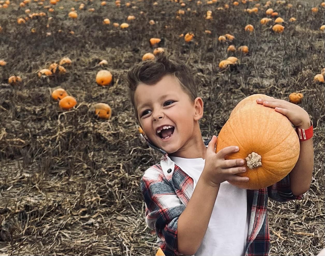 small boy holding a pumpkin with an excited smile on his face.
